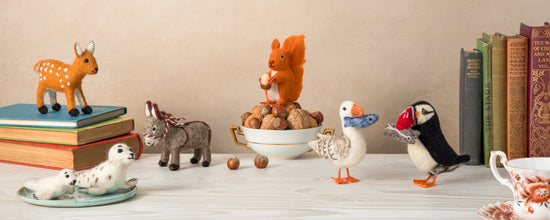 A group of handmade felt British wildlife animals by Sew Heart Felt, including a squirrel, deer, seal and puffin, on a warm brown autumnal background